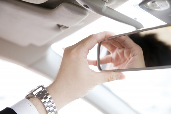 A man reaching up to adjust a rear-view mirror