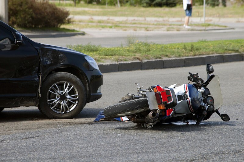 Después de un accidente, una motocicleta yace en la calle junto a un coche averiado