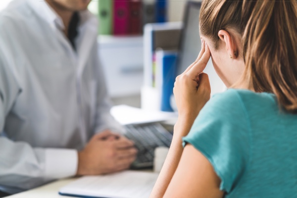  Una mujer está hablando con un médico mientras sostiene la cabeza adolorida.