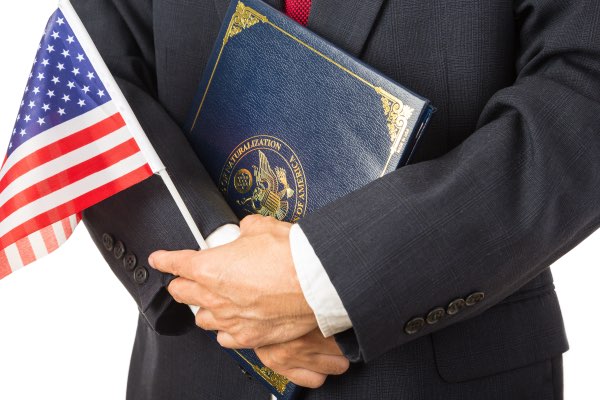 A man is holding an American flag and a new citizenship packet.