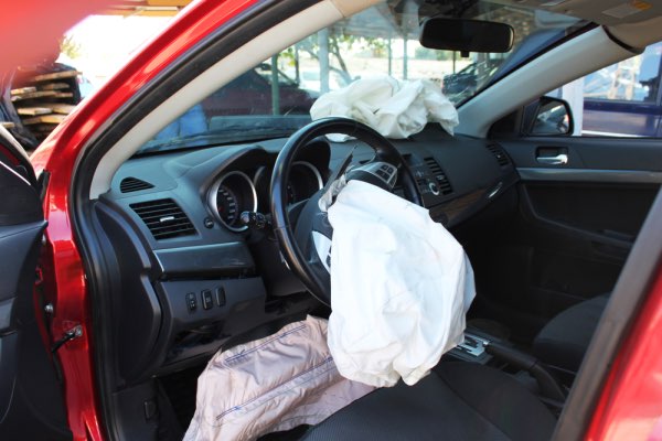 Un primer plano de un automóvil rojo con las bolsas de aire desplegadas.